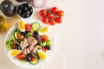Fresh Caesar tuna salad with delicious tuna fish, ruccola, spinach, cabbage, arugula, egg, parmesan and cherry tomato on wooden background. Oil, salt and pepper. Healthy and diet food concept.