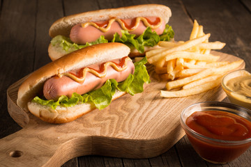 Photo of barbecue grilled hot dog with yellow mustard and ketchup on wooden background. Hot dog sandwich with potato fries and sauces.