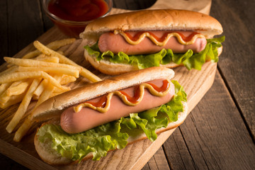 Photo of barbecue grilled hot dog with yellow mustard and ketchup on wooden background. Hot dog sandwich with potato fries and sauces.