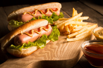 Photo of barbecue grilled hot dog with yellow mustard and ketchup on wooden background. Hot dog sandwich with potato fries and sauces.
