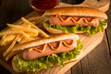 Photo of barbecue grilled hot dog with yellow mustard and ketchup on wooden background. Hot dog sandwich with potato fries and sauces.