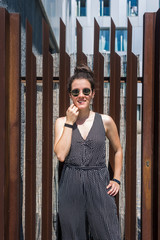 Pretty young stylish woman wearing sunglasses  standing against a fence