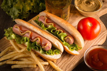 Photo of barbecue grilled hot dog with yellow mustard and ketchup on wooden background. Hot dog sandwich with potato fries and sauces.