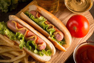 Photo of barbecue grilled hot dog with yellow mustard and ketchup on wooden background. Hot dog sandwich with potato fries and sauces.