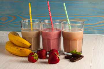 Long glasses of milkshakes with chocolate, strawberry, banana, with ice cream on white and blue...