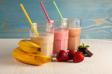 Long glasses of milkshakes with chocolate, strawberry, banana, with ice cream on white and blue...