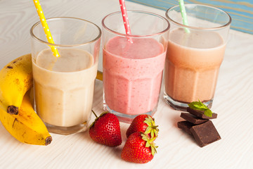 Long glasses of milkshakes with chocolate, strawberry, banana, with ice cream on white and blue background. Shakes and smoothies. Milk shake and cocktail for summer.