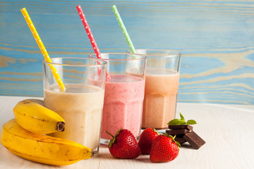 Long glasses of milkshakes with chocolate, strawberry, banana, with ice cream on white and blue background. Shakes and smoothies. Milk shake and cocktail for summer.