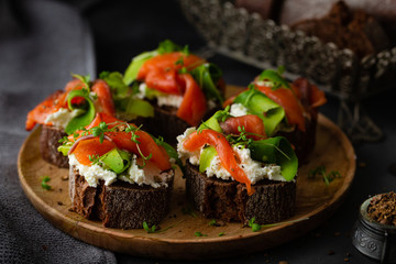 Homemade toast sandwich with rye bread, salmon, avocado, cottage cheese and microgreen sprouts on dark board background. healthy food - breakfast close-up