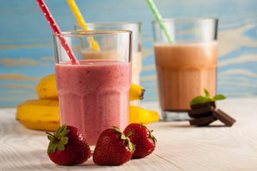 Long glasses of milkshakes with chocolate, strawberry, banana, with ice cream on white and blue background. Shakes and smoothies. Milk shake and cocktail for summer.