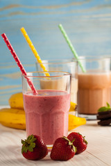 Long glasses of milkshakes with chocolate, strawberry, banana, with ice cream on white and blue background. Shakes and smoothies. Milk shake and cocktail for summer.