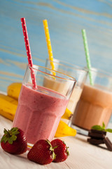 Long glasses of milkshakes with chocolate, strawberry, banana, with ice cream on white and blue background. Shakes and smoothies. Milk shake and cocktail for summer.
