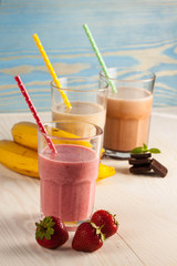 Long glasses of milkshakes with chocolate, strawberry, banana, with ice cream on white and blue background. Shakes and smoothies. Milk shake and cocktail for summer.
