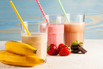 Long glasses of milkshakes with chocolate, strawberry, banana, with ice cream on white and blue background. Shakes and smoothies. Milk shake and cocktail for summer.