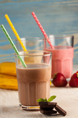 Long glasses of milkshakes with chocolate, strawberry, banana, with ice cream on white and blue background. Shakes and smoothies. Milk shake and cocktail for summer.