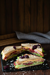A club sandwich on a dark table with ham, cheese, bacon and lettuce close-up.