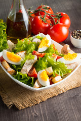 Fresh Caesar salad with delicious chicken breast, ruccola, spinach, cabbage, arugula, egg, parmesan and cherry tomato on wooden background. Oil, salt and pepper. Healthy and diet food concept.