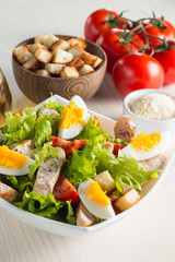 Fresh Caesar salad with delicious chicken breast, ruccola, spinach, cabbage, arugula, egg, parmesan and cherry tomato on wooden background. Oil, salt and pepper. Healthy and diet food concept.