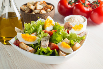 Fresh Caesar salad with delicious chicken breast, ruccola, spinach, cabbage, arugula, egg, parmesan and cherry tomato on wooden background. Oil, salt and pepper. Healthy and diet food concept.