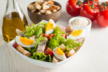Fresh Caesar salad with delicious chicken breast, ruccola, spinach, cabbage, arugula, egg, parmesan and cherry tomato on wooden background. Oil, salt and pepper. Healthy and diet food concept.