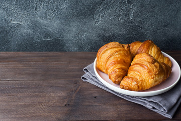 Freshly baked croissants on a plate, dark background, copy space.