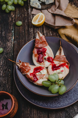 baked pears with blue cheese and prosciutto ham in bowl  with lemons. grape and textile on wooden background
