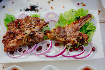 Barbecue ribs on white plate, meat dish served with onion and herbs.