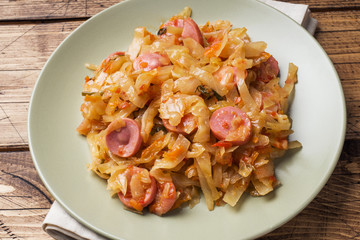 Stewed cabbage with sausages in a plate on the table. Selective focus.