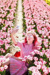 Young woman wear sunglasses make selfie in tulips flower field in sunny spring day