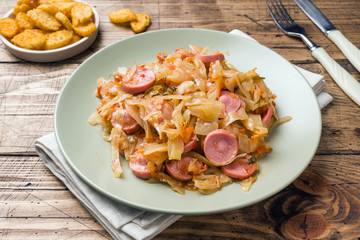 Stewed cabbage with sausages in a plate on the table. Selective focus.