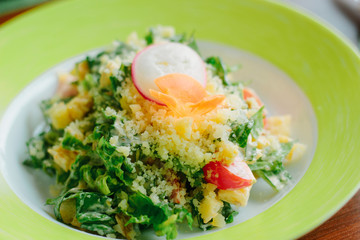 Salad with radish, carrot, lettuce and cheese in a green plate.