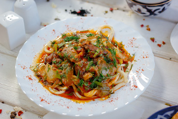Uyghur lagman with fresh meat and vegetables on white plate.