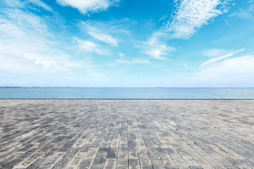 Empty brick floor and blue lake with sky clouds
