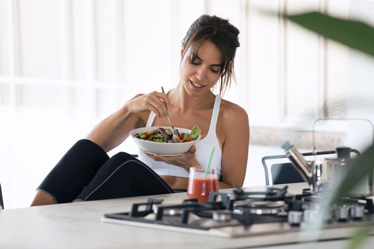 Sporty Young Woman Eating Salad And Drinking Fruit Juice In The Kitchen At Home.