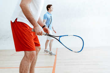 Partial view of two squash players with rackets in four-walled court