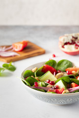 Healthy classical vegetable fresh salad of spinach, tomato, cucumber, onion, cashew nuts, pomegranate and sesame with olive oil dressing on white plate and white background. Diet menu.