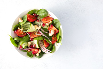 Top view of healthy classical vegetable fresh salad of spinach, tomato, cucumber, onion, cashew nuts, pomegranate and sesame with olive oil dressing on white plate and white background. Diet menu.