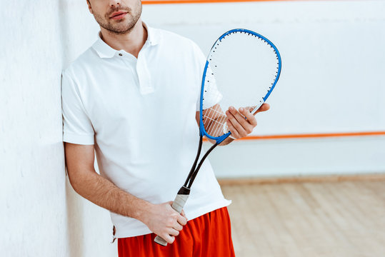 Partial view of bearded squash player holding racket in four-walled court