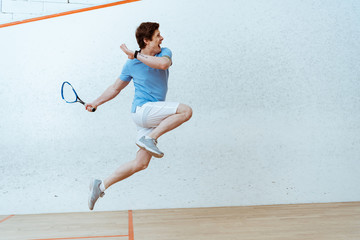 Sportsman in polo shirt jumping while playing squash in four-walled court