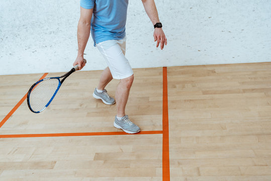 Partial view of sportsman with racket playing squash in four-walled court