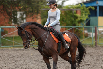 Young girl riding bay horse on equestrian sport training
