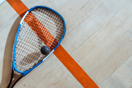 Top view of squash racket and ball on wooden surface