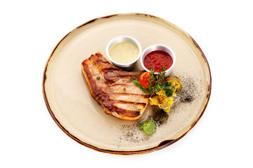 Grilled pork steak served on a plate with vegetables and sauce isolated at white background.
