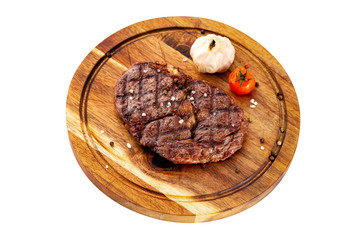 Ribeye steak served with tomato and garlic at a wooden board isolated at white background.