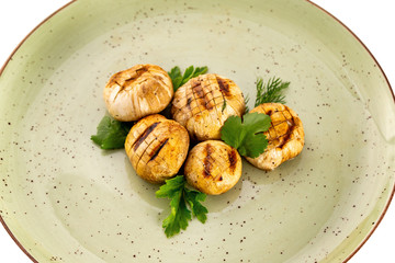 Plate of grilled champignon mushrooms served with green isolated at white background.