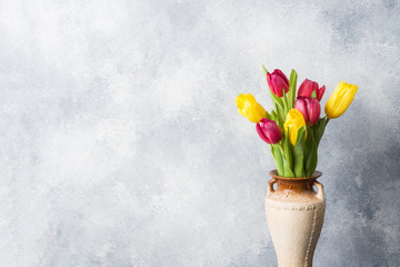 Bouquet of yellow and pink tulips in vase on a gray background. Copy space for product and text.