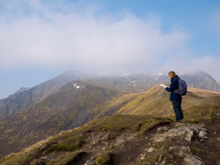 Naklejka na ściany i meble A lone walker looks at a map on the way to the misty summit of Blencathra (also known as Saddleback) in the Lake District, Cumbria, UK with cloud falling against a blue sky