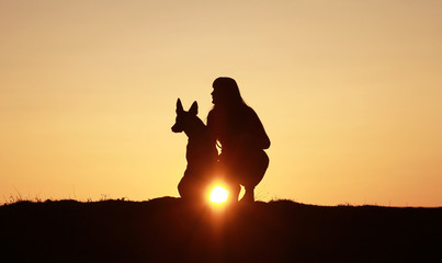 Fototapeta na wymiar Silhouette of a girl and a dog on the background of a beautiful sunset, a breed of Belgian Shepherd dog Malinois