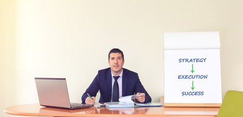 Young successful business man at office desk writing paperwork and using laptop 