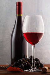 A glass of red wine with grapes and a bottle on a wooden table.
